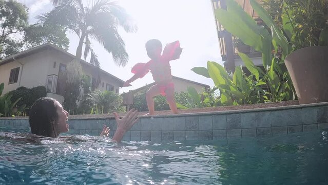 Toddler girl jumps into pool with arm floaties on bright summer day
