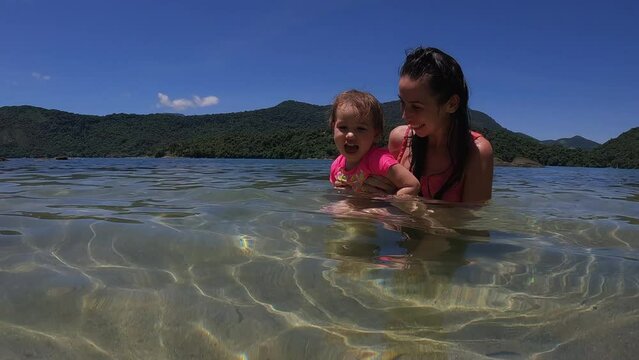 Mother and toddler daughter enjoying tropical ocean waters on vacation - wide shot