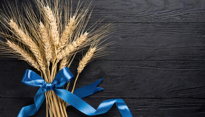  Top view of wheat ears bouquet with blue ribbon placed on textured black wooden plank