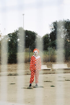 scary clown outdoors seen through a fence, 35mm