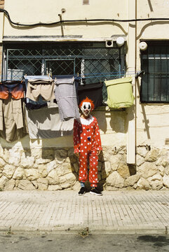 scary clown standing on the sidewalk of a street, 35mm