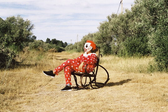 clown sitting on a rocking chair outdoors, 35mm