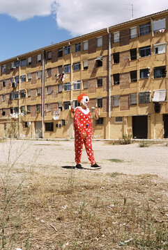 clown walking by a vacant lot in front of an apartment block, 35mm