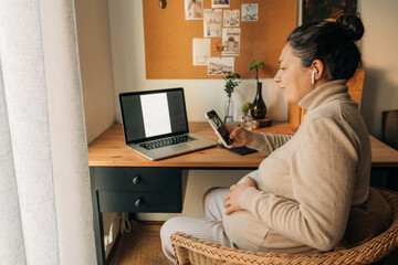 Pregnant woman looking at her phone sitting at the desk