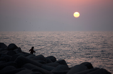 Sunset view with the silhouettes of fishing people on the seawall