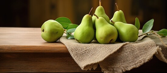 A cluster of small green Willians Pears or Bartlett Pears resting on a rustic wooden table, with a backdrop of textured fabric adding to the natural aesthetic of the scene.