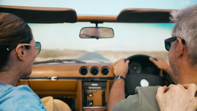 Close up of retired senior couple on vacation driving in classic sports car on road trip through countryside - shot in slow motion