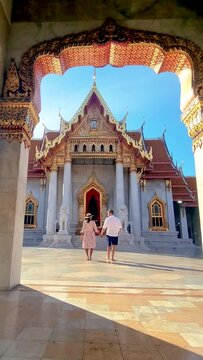 A couple stands hand in hand in front of a majestic temple, admiring the intricate facade of the building. symmetry architecture enhances romantic moment Wat Benchamabophit temple, Bangkok, Thailand