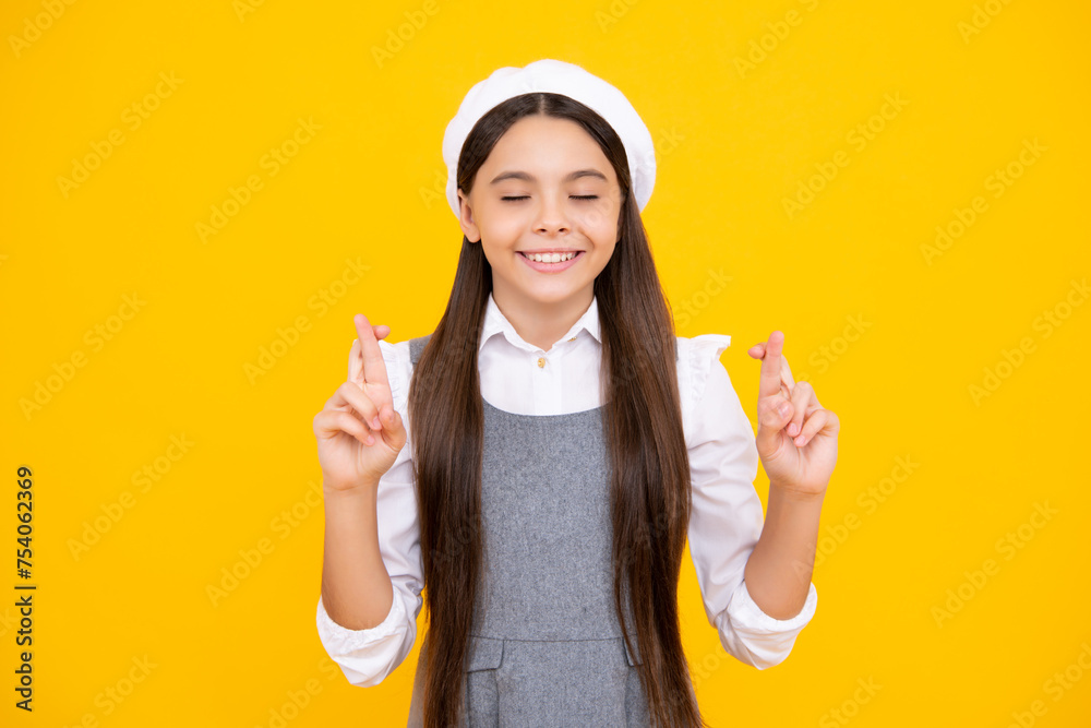 Poster portrait of adorable little teenager gitl standing with closed eyes and crossing fingers, wishing fo