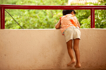 A young boy in an orange shirt and white shorts is leaning over a railing - Powered by Adobe