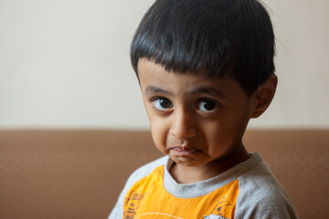 A young boy with a yellow shirt is looking at the camera with a frown on his face