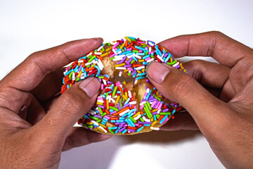 one donut with colorful sprinkle topping, held in the left hand, on a plain white backgorund