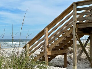 A wooden walkway and stairs lead to the beach, adjacent to the dunes, with sea grass, ocean waves, and the expansive sky at Ponce Inlet, FL.