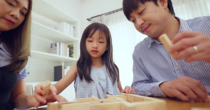Asian family with young daughter enjoying a wooden board game in a bright, cozy home setting.