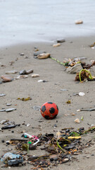 A solo red and black football washed up from ocean onto polluted sandy beach on a tropical island