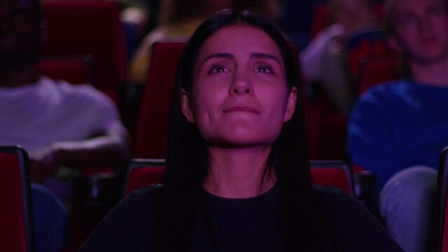 A woman shed tears from watching a film in a cinema, a woman watches the premiere in a cinema and shed tears from a powerful scene, tears appeared in the eyes of a young woman in a cinema.