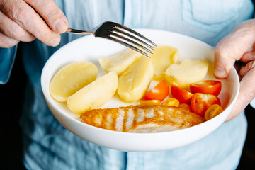 A man holds a plate of potatoes, chicken and tomatoes.