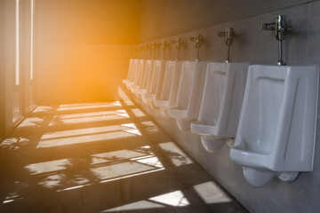 Group of white male urinals in clean public toilet with sun light and shadow. Men restroom with no people background.