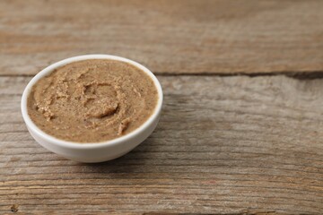 Delicious nut butter in bowl on wooden table, closeup. Space for text