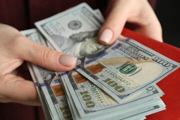 Money exchange. Woman putting dollar banknotes into wallet, closeup view