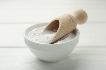 Baking powder in bowl and scoop on white wooden table, closeup