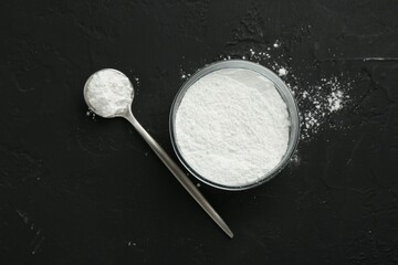 Baking powder in bowl and spoon on black textured table, top view