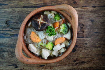 Kaeng Jued Woon Sen, a Thai glass noodle soup brimming with tender chicken and fresh vegetables, served in a classic earthenware bowl for a touch of rustic elegance.