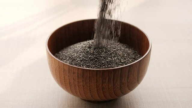 Discover goodness of nutritious chia seeds as its pour into bowl creating healthy snack Watch as chia seeds gracefully fill bowl Enjoy health benefits of chia seeds in satisfying and nourishing bowl