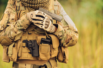 A close-up of a soldier's handgun is ready to load ammunition to shoot at enemies on the battlefield and has an ammunition pouch attached to his camouflage uniform, wearing gloves, a backpack.