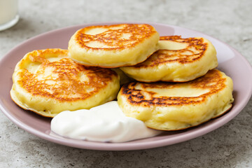 pancakes with sour cream. on a stone gray table there is a white plate with fried pancakes and sour cream, close-up, food concept