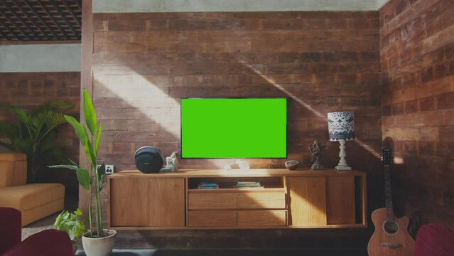 Modern cozy interior of country house with large comfortable sofa and tv with green screen hanging on brick wall near wooden bedside table houseplant with guitar. Apartment, home, mansion