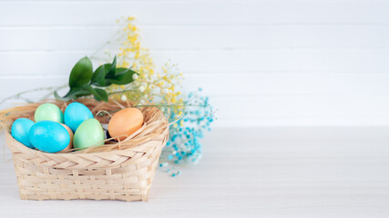 Banner. Easter eggs, feathers in a nest on a white wooden background. The minimal concept. Card with a copy of the place for the text.