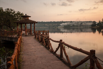 Fototapeta premium A wooden bridge spans a body of water, with a sunset in the background, Mandu, India.