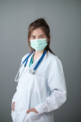 Young Asian female doctor standing on grey background.