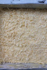 Indonesian food called prol tape sprinkled with cheese in a baking pan ready to be baked on the table