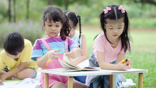 Little boy and girl were having fun drawing pictures and read book, Group of children playing and on sunny summer day in the park, holiday relaxation concept, picnic in summer park, outdoor education