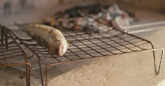 Male cook hand puts fresh raw mullet fish on grill barbeque close up