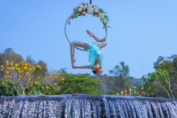 Beautiful Asian girl performing show aerial hoop or aerial ring in various positions and spinning stunts on the blue sky. © pomphotothailand