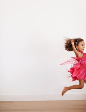 Girl, space or child in costume running with confidence, wellness or fairy outfit on wall background. Home, alone or excited kid with speed, youth and hair in the air for mockup, activity or jumping