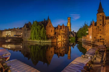 Fototapeten Center of the old town of Bruges with a view of the Rosary Quay. Old Belgian Hanseatic town with canal at blue hour. Reflections of illuminated historic merchant houses and belfry on the water surface © Marco