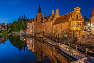 Fototapeta na wymiar Evening atmosphere in Bruges at the Rosary Quay canal. Illuminated historic buildings of the old town. Reflections of old merchant houses on water surface. Boats at the jetty