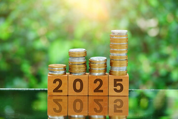Pile of coins on wooden cubes with engraved number 2025 with reflection and bokeh nature...