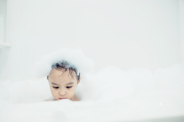 Cute little girl taking bath playing with foam and soap bubbles. Hygiene for infant and baby. Soft focus. Copy space.	