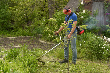 Man mowing grass with petrol lawn trimmer in garden