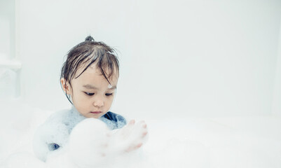 Cute little girl taking bath playing with foam and soap bubbles. Hygiene for infant and baby. Soft focus. Copy space.	