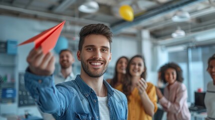The happy male leader of the company threw a red paper airplane into the office. There was a group of employees smiling and talking in the background. - obrazy, fototapety, plakaty