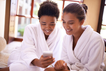Beauty, phone and spa with woman friends in robes for luxury pampering or treatment together. Smile, app and social media with happy young people at resort or salon for wellness or weekend getaway