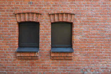 Wall of an ancient building made of red brick. There are 2 windows covered with modern brown panels. Background. Form