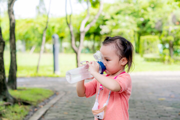 Little asian girl drinking water in garden park. Summer day. Copy space.	