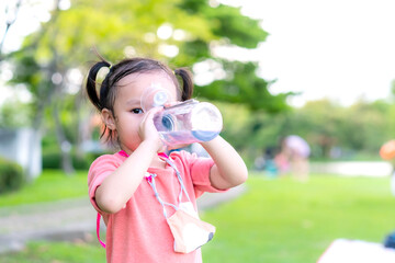 Little asian girl drinking water in garden park. Summer day. Copy space.	